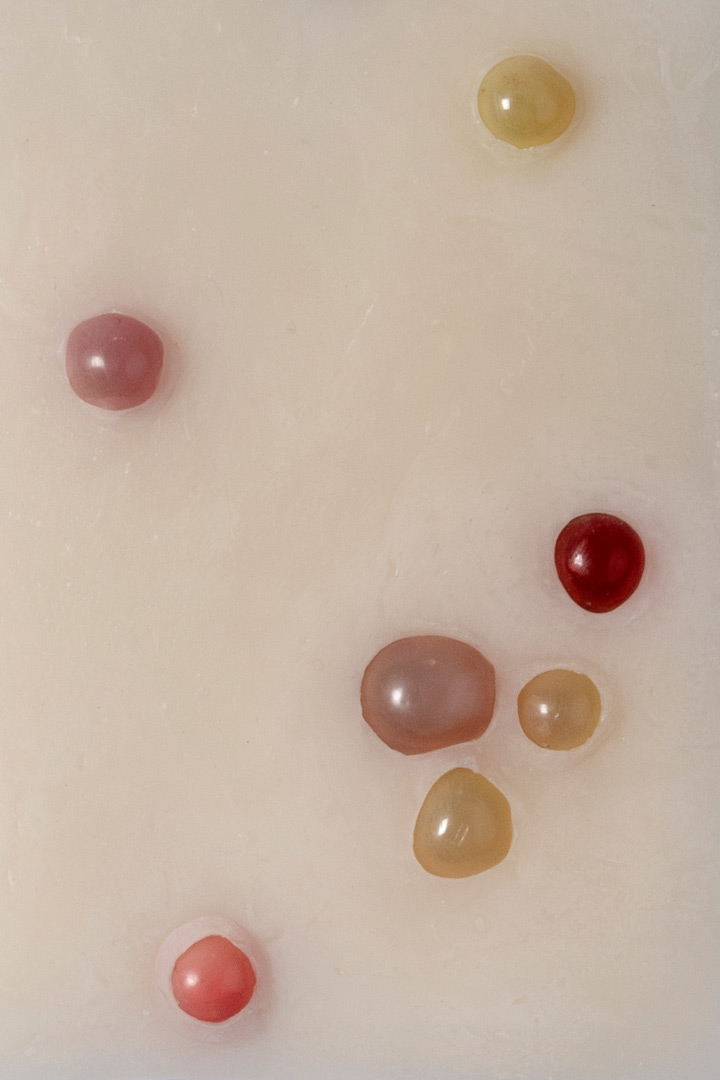 Fragment de l'installation Spleen Spring. Focus sur une forme en cire rectangulaire ponctuée de sept billes jaunâtres, rougeâtres et rosâtres évoquant l'acné.