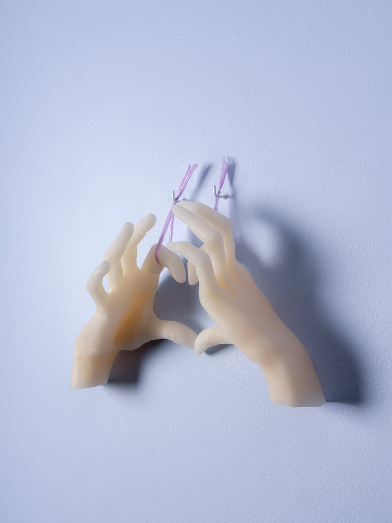 Fragment de l'installation Spleen Spring. Focus sur une forme en cire photographiée de trois-quarts. La forme est un moulage d'une paire de mains positionnée de manière à former un cœur avec les doigts.
