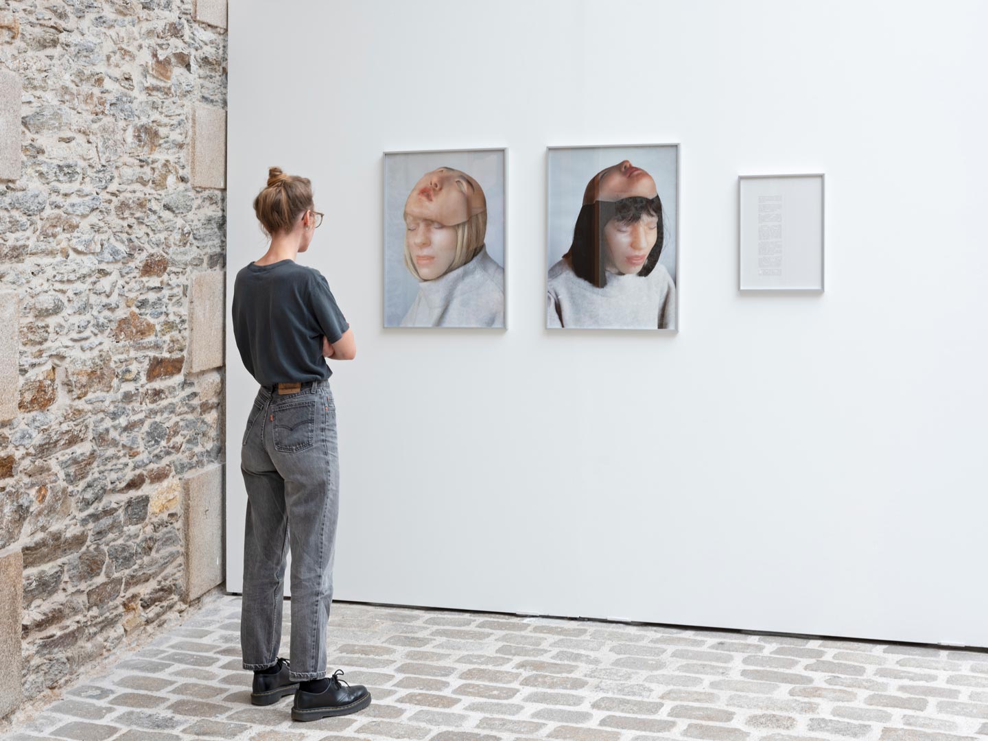 Vues d'exposition montrant une personne regardant un ensemble de deux photographies de grand format accompagné d’un texte.