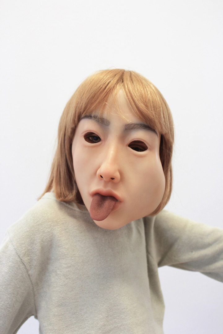 Vue d'exposition de l'installation intitulée "Les Vieux démons". Focus resserré sur une des figures enfantines, portant une facette de silicone hyperréaliste en guise de visage et tirant la langue.