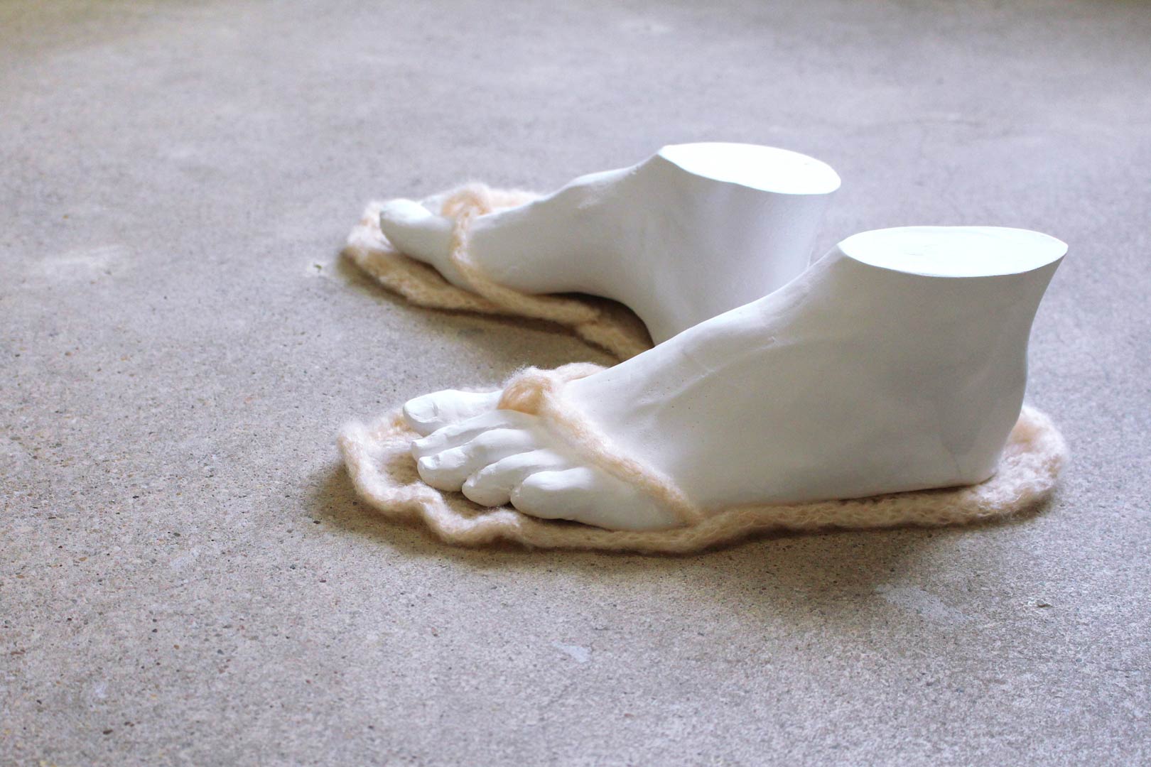 Vues de l'installation intitulée "Douces indolences". Focus resserré sur une paire de pieds sans corps chaussant des tongs en laine rose pale. Les pieds sont issus de moulages en plâtre réalisés à partir des corps des artistes.