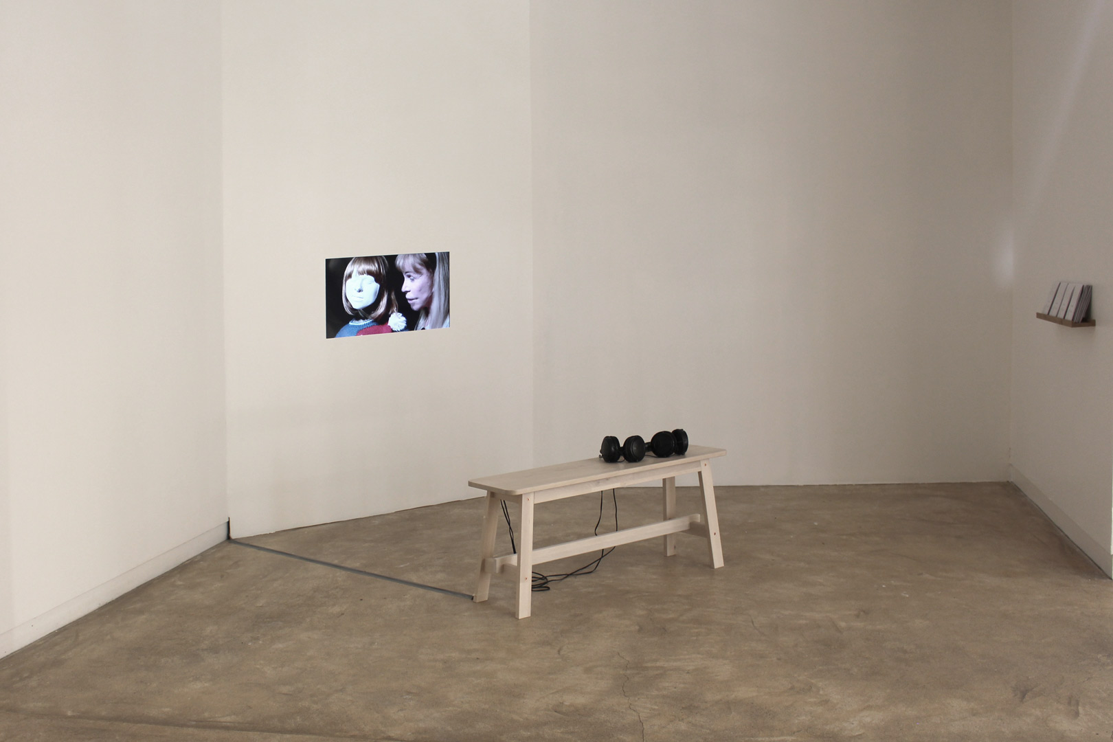 Vue de l'exposition intitulée " J'ai léché l'entour de vos yeux". Vue de la mise en espace de la vidéo "A vous", écran vidéo encastré dans le mur, un banc et deux casques audio.