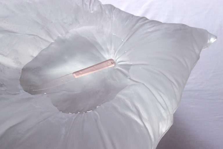 Un couteau rose, transparent est déposé au creux d'une flaque d'eau qui siège dans un oreiller translucide, presque givré.